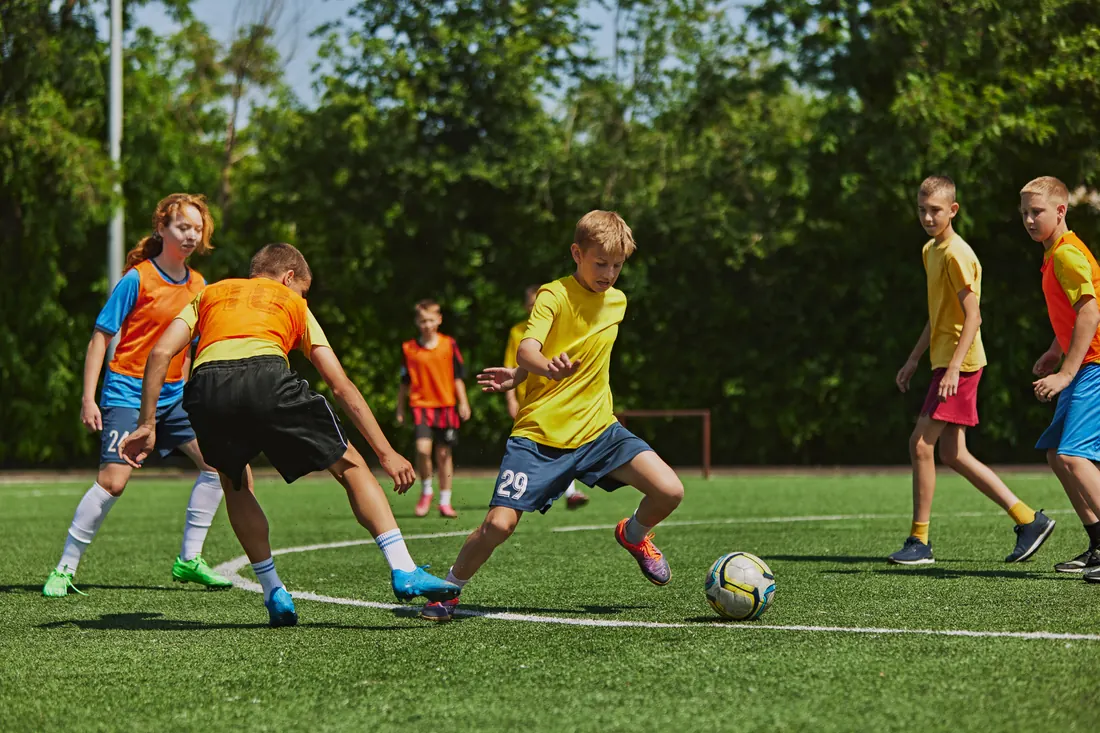 Zweikampf im Jugendtraining: ein Spieler zieht mit dem Ball
                  an zwei Gegenspielern vorbei, weitere Kinder warten im
                  Hintergrund.